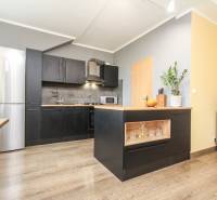 Konyha egy 4 szobás lakásban, szigettel, fekete szekrényekkel és fa dekorációjú padlóval.