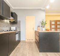 Konyha egy 4 szobás lakásban fekete szekrényekkel és fa mintázatú padlóval.