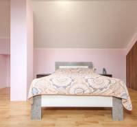 Világos hálószoba, fa mintázatú padló, ferde mennyezet, kényelmes ágy, tárolóhely.