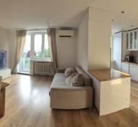 Tágas konyha nappalival egy háromszobás lakásban. Fa hatású padló, világos bútorok.