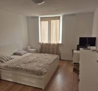 Világos hálószoba egy háromszobás lakásban, ággyal és fa mintázatú padlóval.