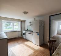 Családi ház konyhája fa mintázatú padlóval, felszerelve háztartási gépekkel és étkezőasztallal.