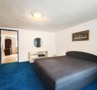 Hálószoba családi házban nagy ággyal, kék szőnyeggel és képpel a falon.