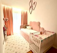 Gyerekszoba egy háromszobás lakásban rózsaszín részletekkel és fa padlóval.