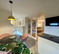 Étkező sarok kerek asztallal, rózsaszín székekkel és érdekes világítással egy háromszobás lakásban.