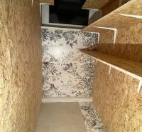 Tárolóhely egy háromszobás lakásban fa polcokkal és virágos tapétával.