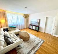 Nappali háromszobás lakásban kanapéval, televízióval és függönyökkel az ablakon.