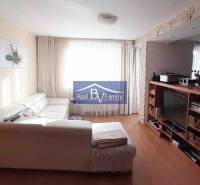 Nappali fehér kanapéval és televízióval, fa hatású padlóval, 2 szobás lakás.