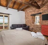 Hálószoba egy villában téglafalakkal, TV-vel, kanapéval és nagy ággyal.