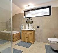 Fürdőszoba káddal, zuhanyzóval, tükörrel és szekrénnyel a házikóban. Világos csempék és padlóburkolat.