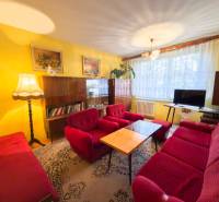 Nappali egy háromszobás lakásban piros kanapékkal, szőnyeggel, faldekorációkkal, fa bútorokkal.