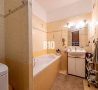 Fürdőszoba sárga csempékkel, káddal, mosdóval és tárolóhellyel egy 4 szobás lakásban.