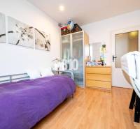 Szoba egy négyszobás lakásban egyszemélyes ággyal, szekrénnyel és fa mintázatú padlóval.