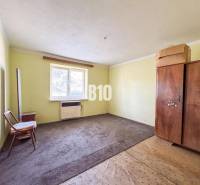 Egyszerű szoba egy családi házban, szőnyeggel és fa bútorokkal.