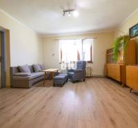 Nappali egy családi házban, fa bútorokkal, szürke kanapéval és világos padlóburkolattal.