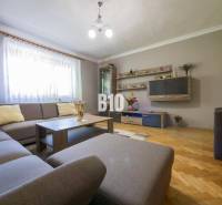 Nappali sarokkanapéval, fa parkettával, dekoratív polcokkal és világítással egy családi házban.