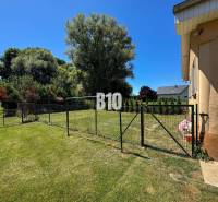 A családi ház kertje Újszádon, bekerített füves terület, fák és bokrok.