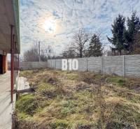 Családi ház építése füves telekkel és kerítéssel, felhős ég alatt.