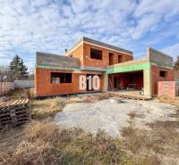 Befejezetlen téglából épült családi ház, amit fű és fa raklapok vesznek körül.