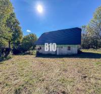 Ház Lackovban, természettel körülvéve, kék tetővel, napos nap.