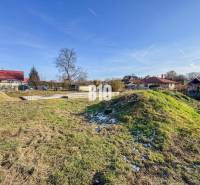 Építkezésre előkészített telek, havas fű, házakkal és tetőfedésekkel körülvéve.