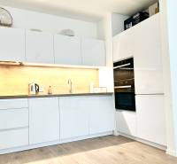 Konyha egy kétszobás lakásban fehér szekrényekkel és fa mintázatú padlóval.