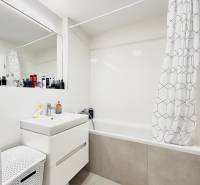 Fürdőszoba káddal és függönnyel egy kétszobás lakásban, fehér szekrény és szennyeskosár.