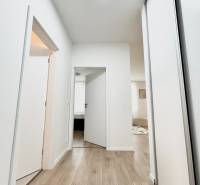 Folyosó világos falakkal és fa dekoros padlóval, amely egy kétszobás lakás helyiségeibe vezet.