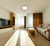 Nappali kanapéval, televízióval, asztallal és fa dekorációjú padlóval egy kétszobás lakásban.