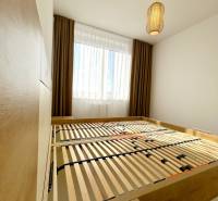 Hálószoba ággyal és lámpával egy kétszobás lakásban, fa mintázatú padlóval.