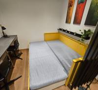 Garzonlakás ággyal, asztallal, székekkel és dekoratív képekkel, fa dekorációjú padlóval.