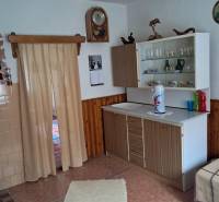 Családi ház belső tere egyszerű konyhával, fa mintázatú padlóval és függönyökkel.