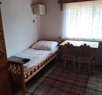 Szoba egy családi házban ággyal, ablakkal, asztallal és székekkel.