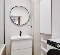 Fürdőszoba egy kétszobás lakásban kerek tükörrel és tárolóhellyel.