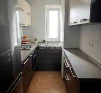 Konyha egy háromszobás lakásban modern szekrényekkel, tűzhely, világos falak, kerámia padló.