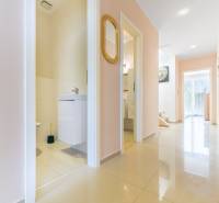 Folyosó a családi házban világos csempékkel, nyitott ajtó a fürdőszobába, tükör a falon.