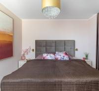 Hálószoba széles ággyal, dekoratív párnákkal, képpel és rejtett tárolóhellyel egy 4 szobás lakásban.