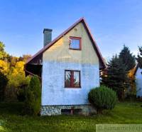 Házikó Sološnicában, zölddel körülvéve, kék vakolattal és ferde tetővel.
