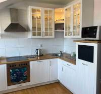 Konyha egy háromszobás lakásban fa padlóval, fehér szekrényekkel és tárolóhellyel.