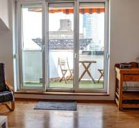 Nappali erkéllyel, fa padló, szék és asztal egy háromszobás lakásban.