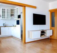 Nappali egy háromszobás lakásban, átjáróval a konyhába és falra szerelt televízióval.