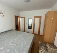 Hálószoba ággyal, szekrénnyel és tükörrel egy családi házban, fa dekoros padlóval.