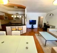 Nappali egy háromszobás lakásban konyhával, étkezőasztallal és kényelmes ülőgarnitúrával.