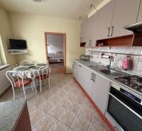 Konyha egy háromszobás lakásban sarok konyhabútorral, asztallal és falra szerelt televízióval.