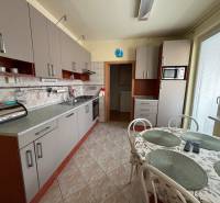 Konyha világosszürke szekrényekkel egy háromszobás lakásban, étkezőasztallal kiegészítve.