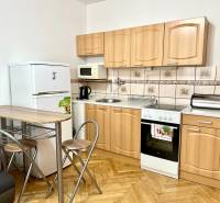 Konyha garzonlakásban fa mintázatú padlóval, háztartási gépekkel és ülőhellyel.