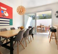 Világos étkező a villában, faasztallal, színes festménnyel és terasszal.