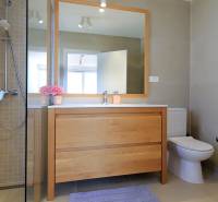 Fürdőszoba a villában fa dekorációval, zuhanyzóval és nagy tükörrel ellátott mosdóval.