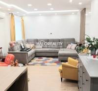 Nappali egy háromszobás lakásban fa dekor padlóval, szürke kanapéval és sárga fotellel.