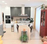 Konyha egy háromszobás lakásban fa dekor padlóval, étkezőasztallal és könyvespolccal.